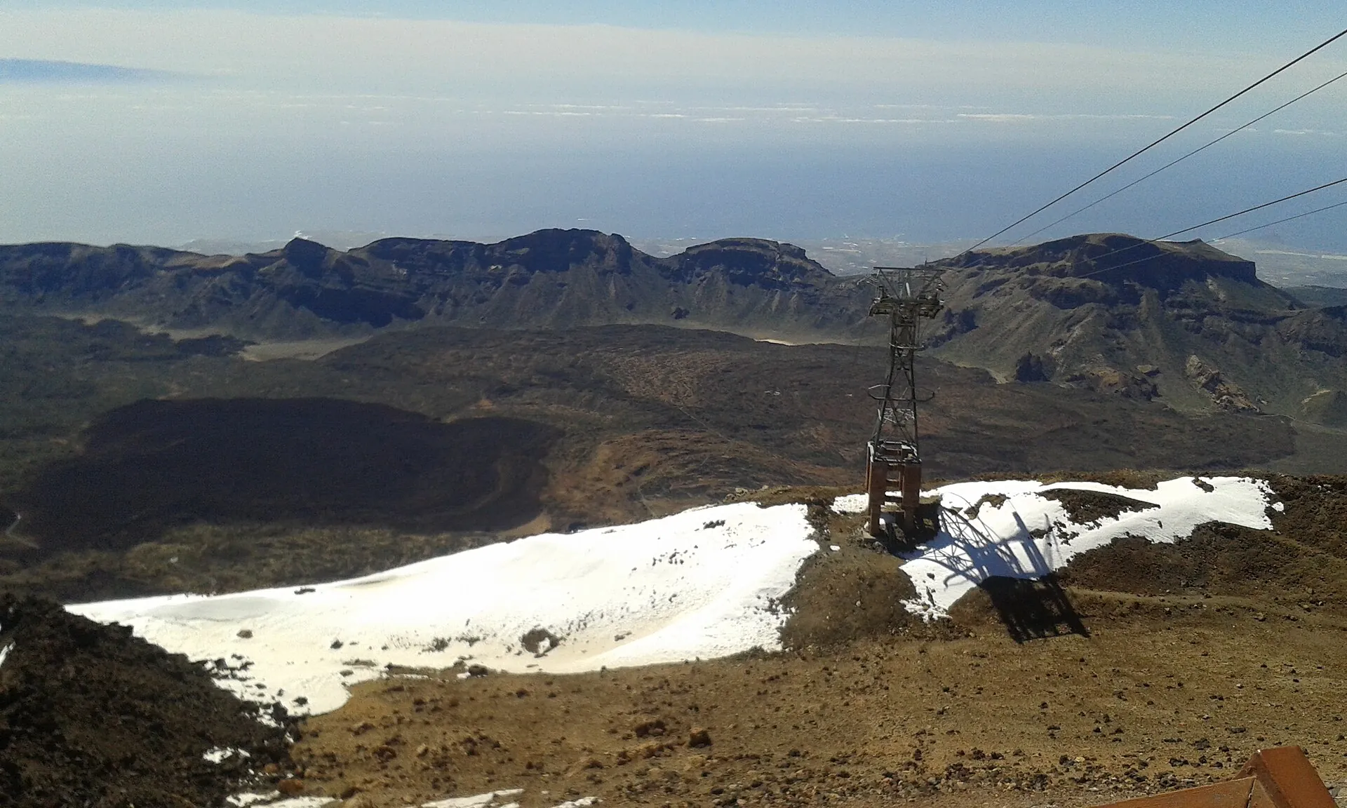 View down from the Teide cable car: the pylon above a snow-covered lava slope, the wide Las Cañadas caldera below