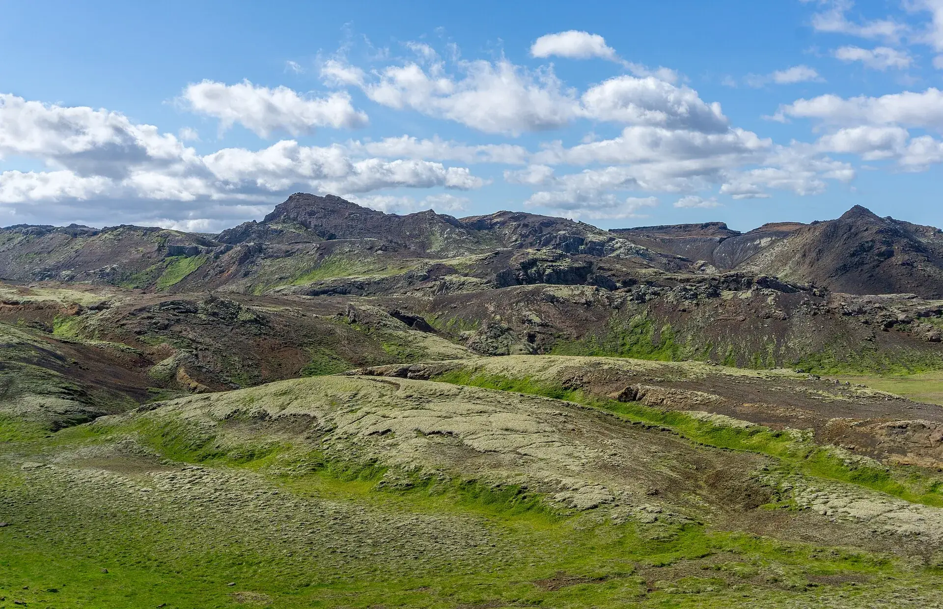Die Bláfjöll vom Wanderweg Reykjavegur: grüne Moosflächen, dunkle Lavarücken und Kegel unter Schönwetterwolken