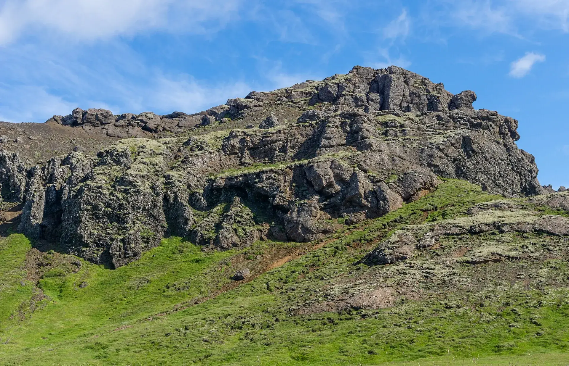 Ein zerklüfteter Lavafelsen in den Bláfjöll, von grünem Moos umgeben, unter blauem Himmel