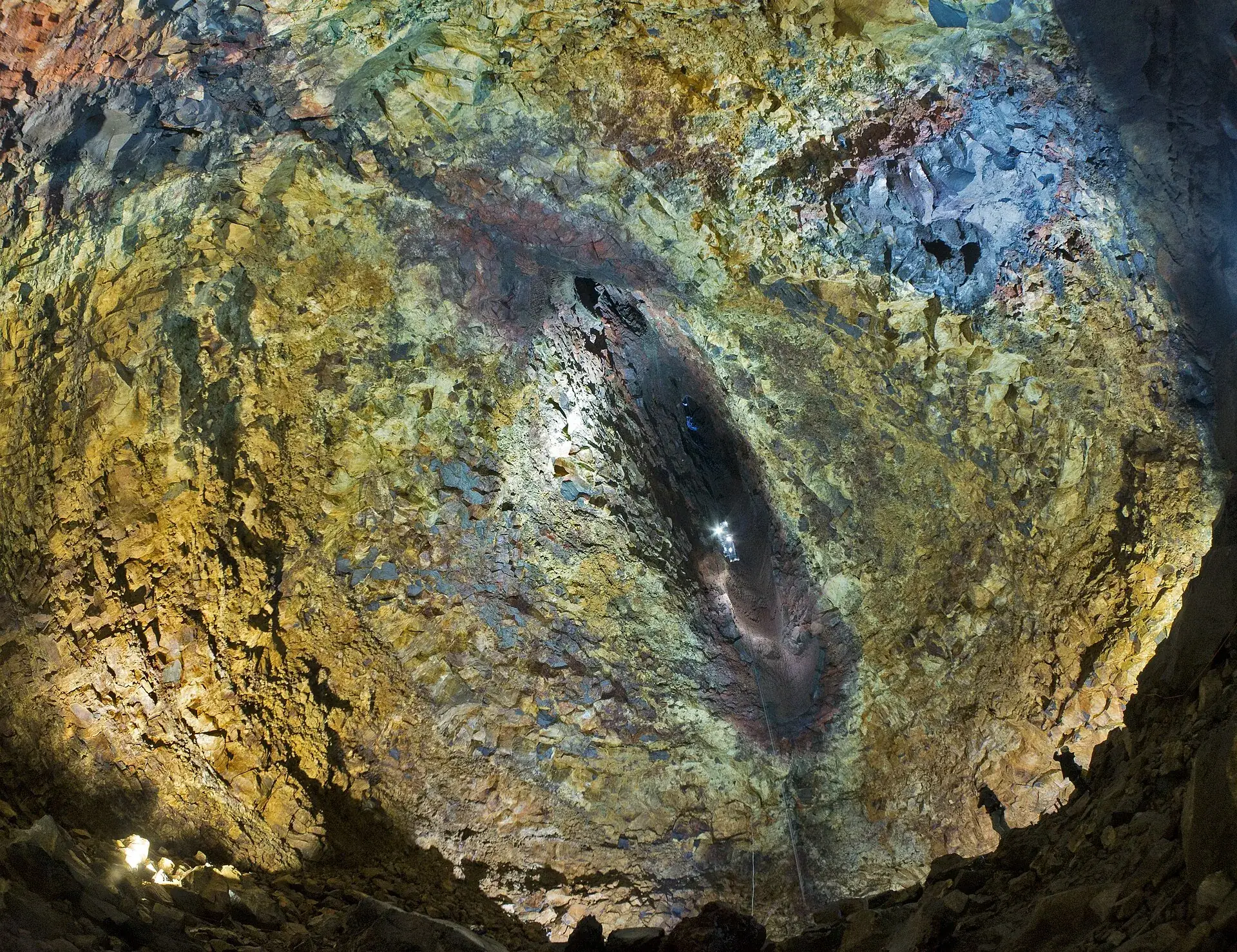 Die Magmakammer des Þríhnúkagígur von unten: rot und gelb gefärbte Wände wölben sich zur Öffnung, durch die ein heller Lichtpunkt fällt
