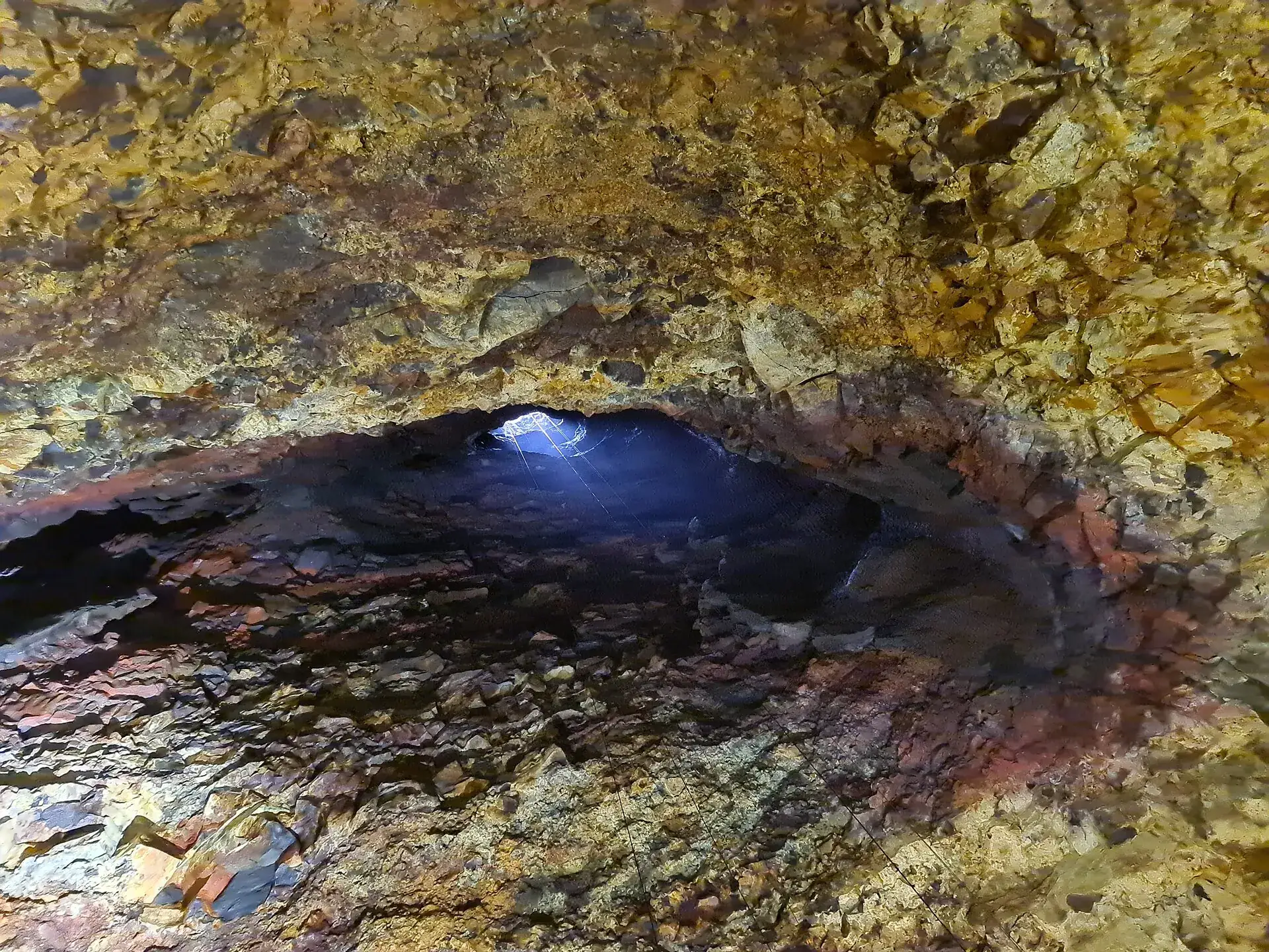 Blick aus der Magmakammer des Þríhnúkagígur nach oben: Tageslicht fällt durch die enge Öffnung auf rot, gelb und schwarz gefärbte Wände