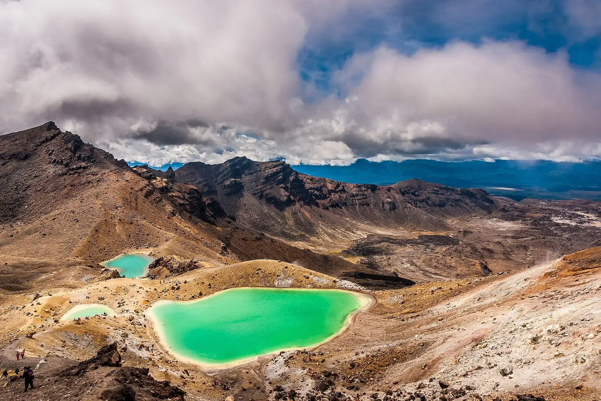 The Emerald Lakes on the Tongariro Alpine Crossing seen from above: three bright green crater lakes among pale scree, clouds overhead