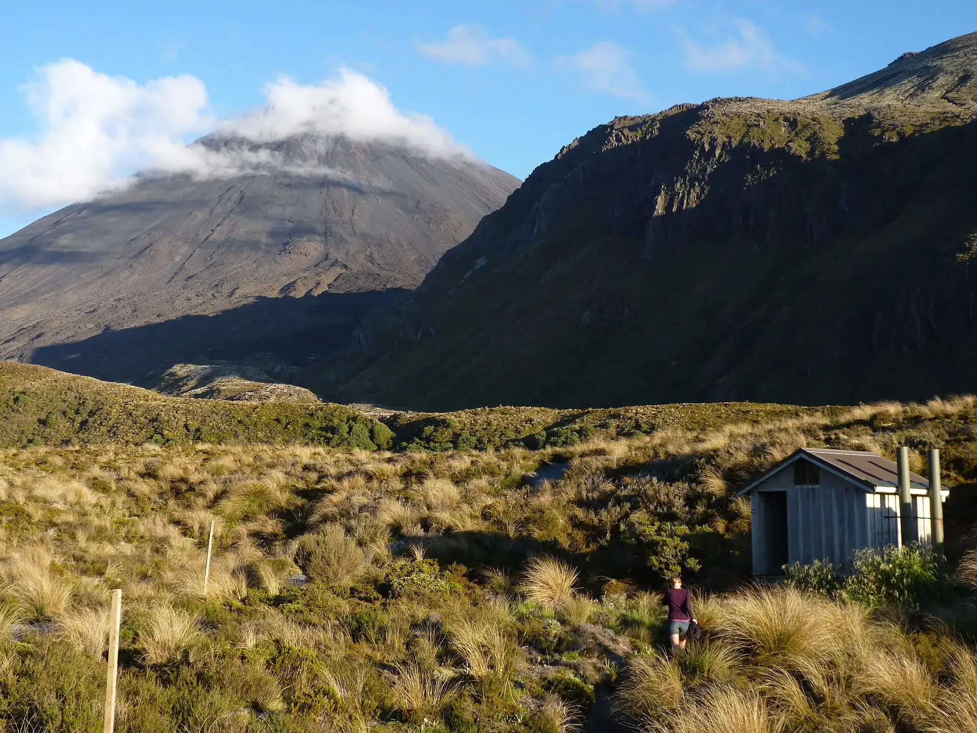 The Mangatepōpō valley in Tongariro National Park in the morning: tussock grass, a hut beside the track, and the cone of Ngāuruhoe behind it under a cap of cloud