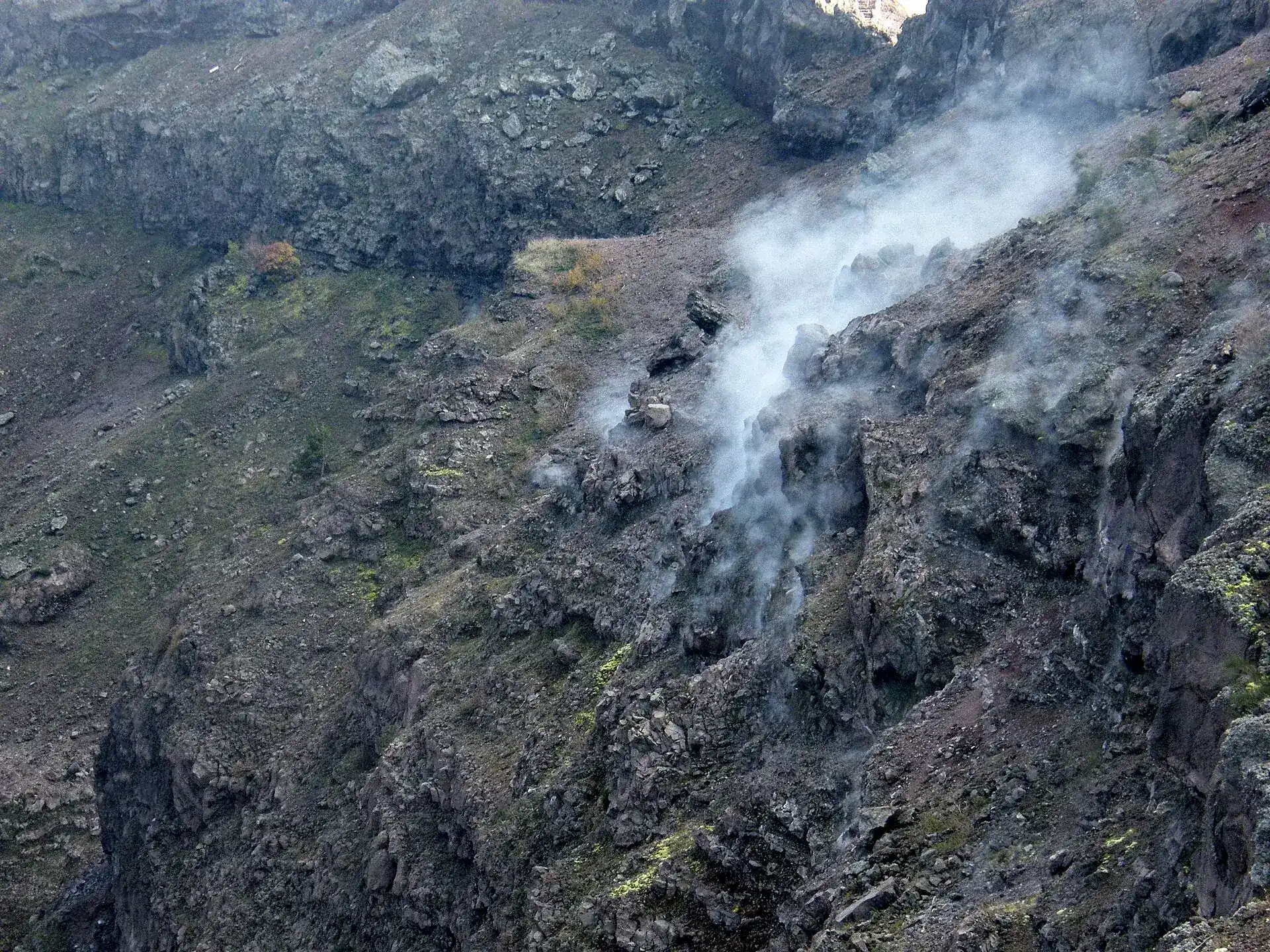 Fumaroles inside the crater of Mount Vesuvius: white steam rising from the dark inner wall