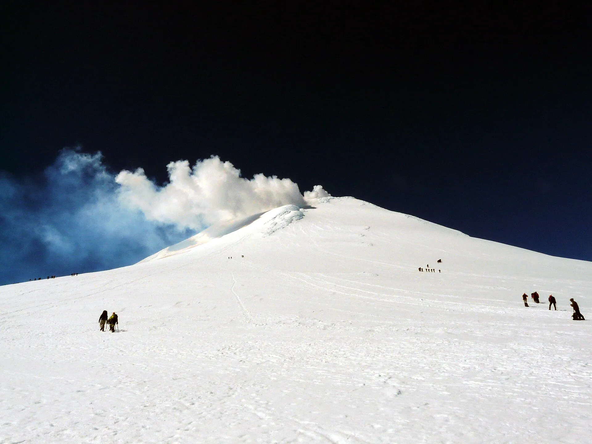 Bergsteiger in kleinen Gruppen auf dem Firnhang kurz unter dem Gipfel des Villarrica, aus dem Krater steigt Dampf
