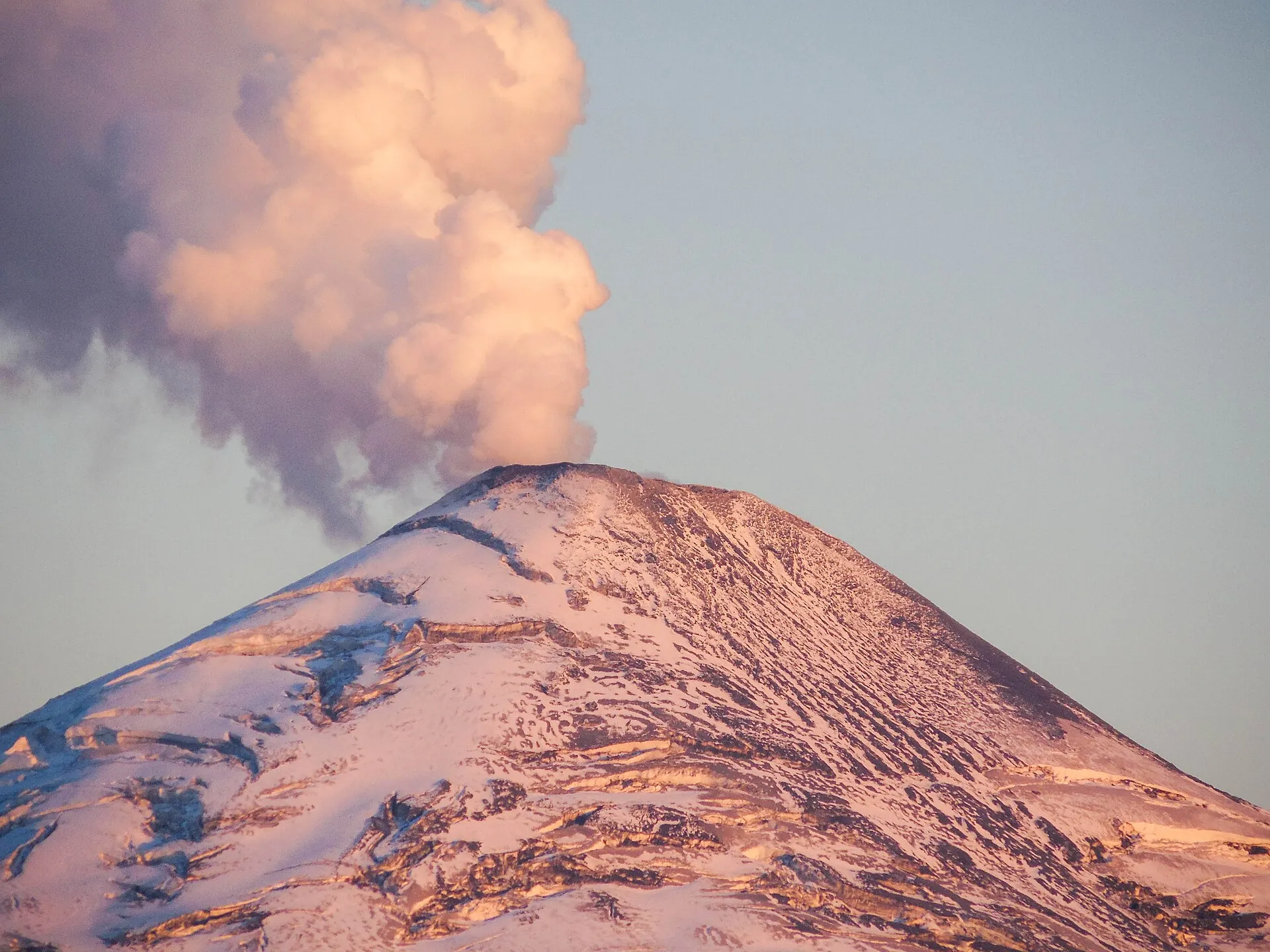 Der Villarrica im Abendlicht, der Schneekegel rosa gefärbt, eine mächtige Dampfwolke steigt aus dem Krater