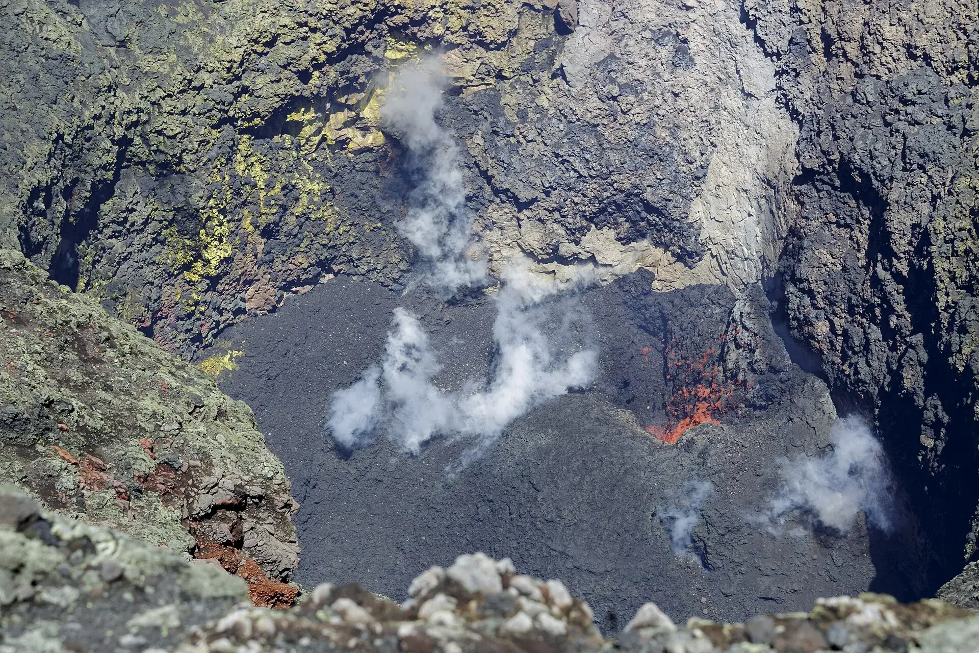 Blick in den Krater des Villarrica: schwarze Lavakruste, weißer Dampf und rotes Glühen aus dem Schlot