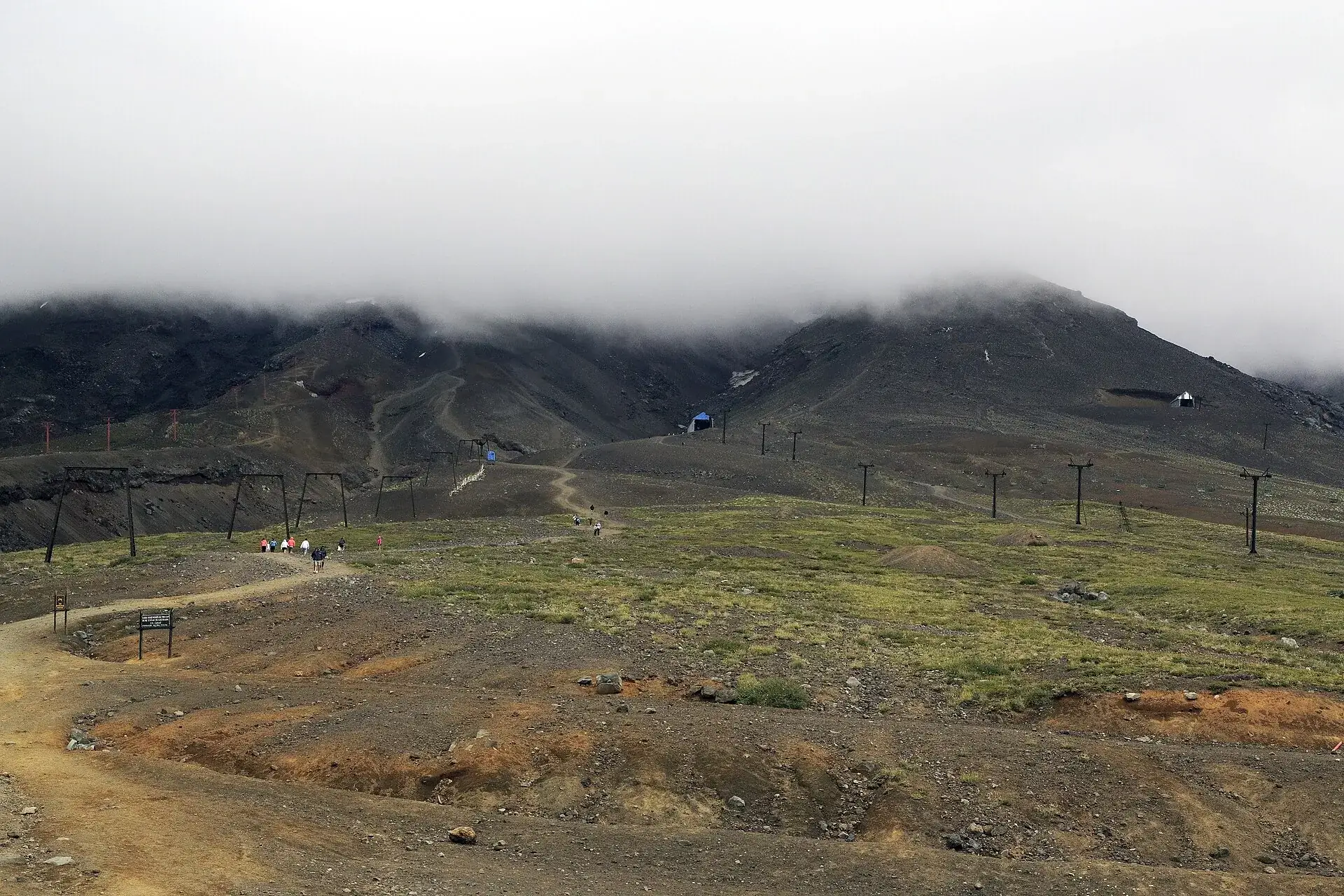 Die Sessellifte des Centro de Montaña Pillán ziehen über schwarzen Vulkansand bergauf, der Gipfel des Villarrica steckt in Wolken