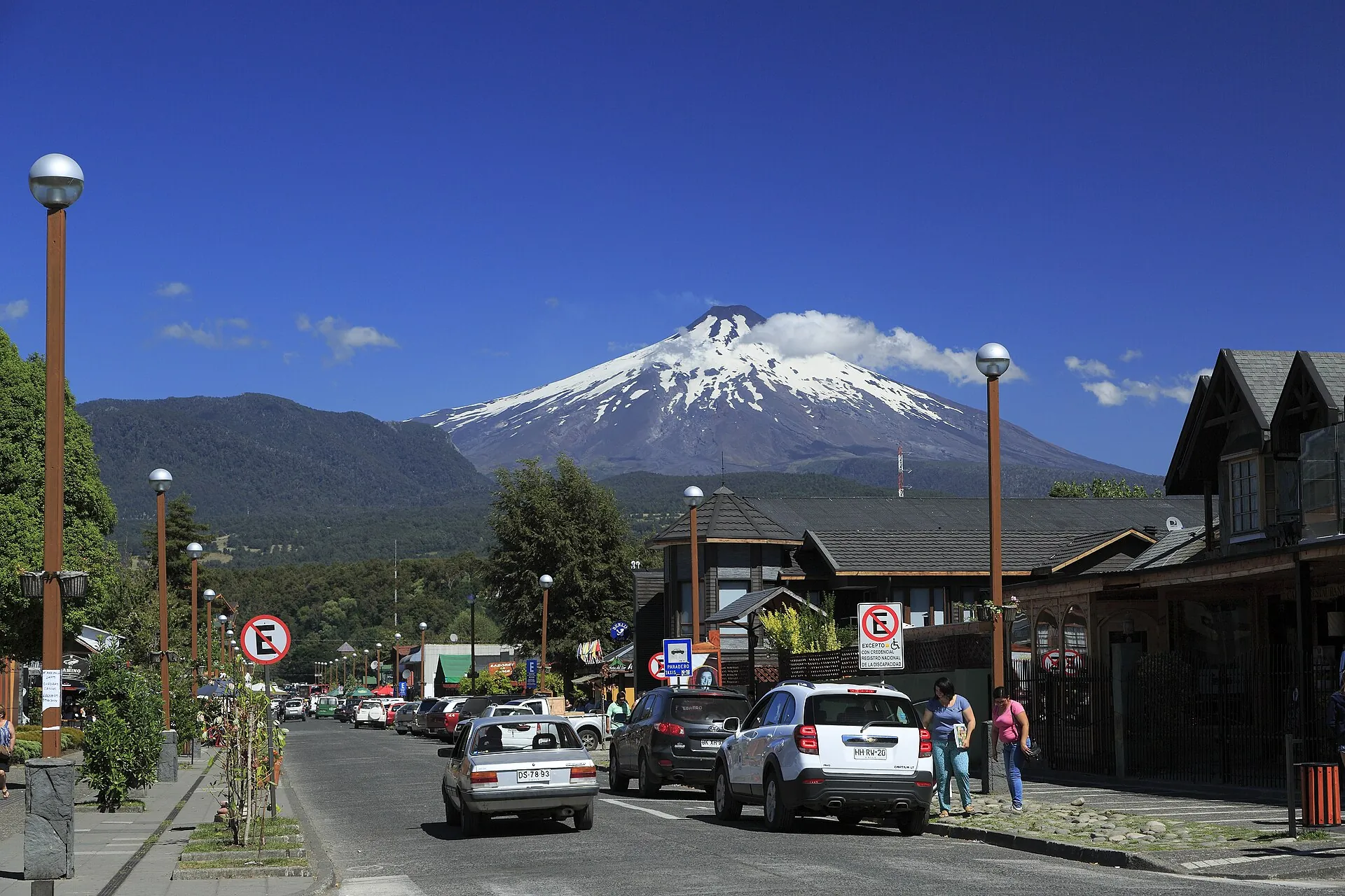 Eine Straße in Pucón mit Autos und Holzhäusern, am Ende der Straße der schneebedeckte Villarrica