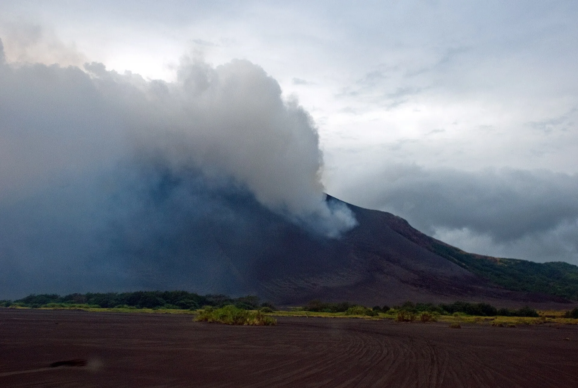 Annäherung an den Mount Yasur über die graue Ascheebene auf Tanna, der Kegel liegt unter einer Dampffahne