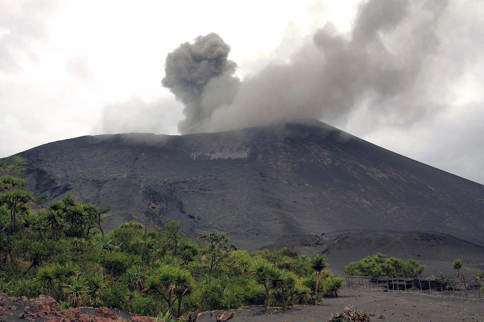 Eine dunkle Aschewolke quillt aus dem Krater des Mount Yasur in den blauen Himmel über Tanna