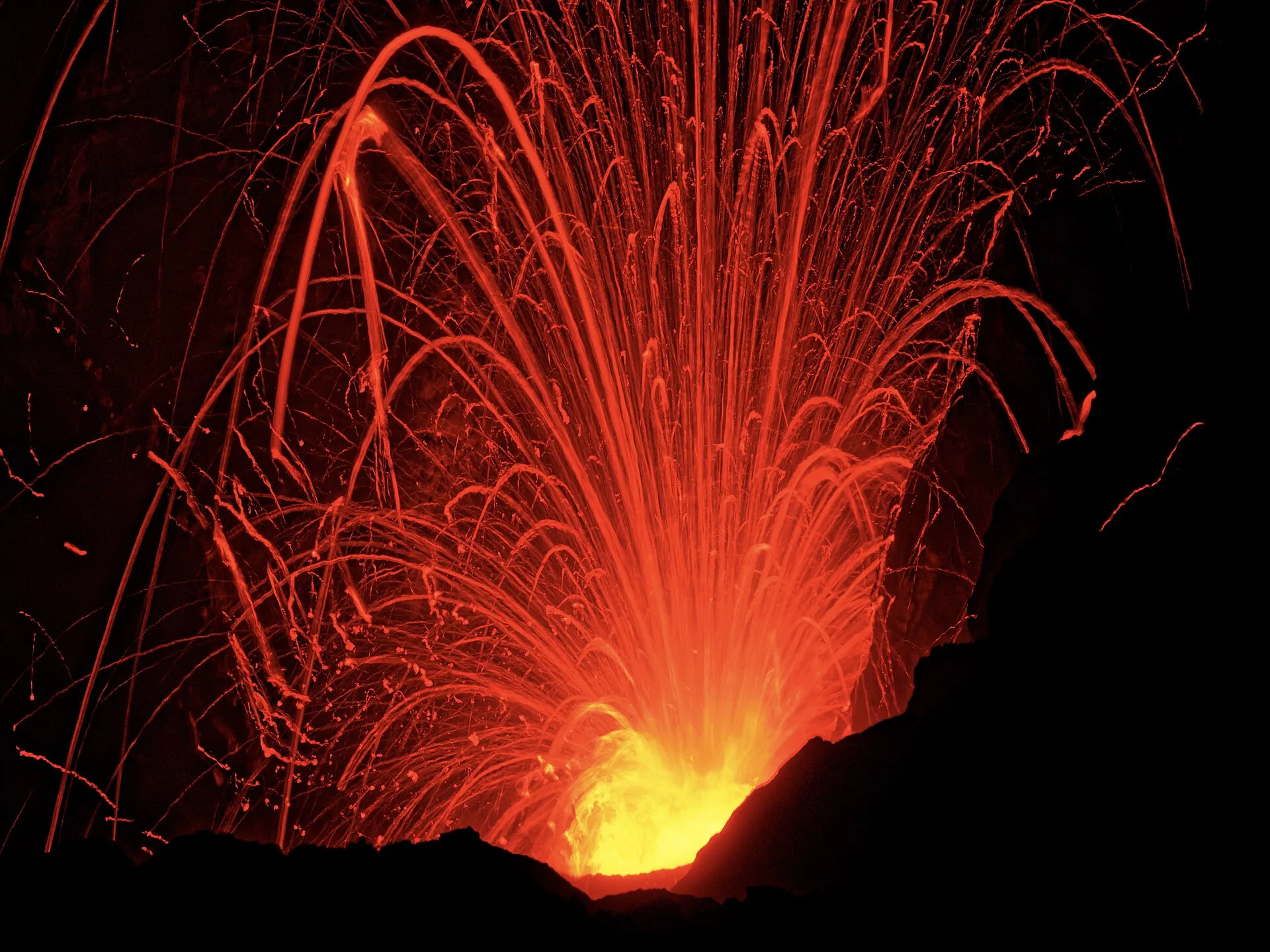 Langzeitaufnahme am Mount Yasur: glühende Lavabahnen zeichnen Bögen über dem dunklen Kraterrand