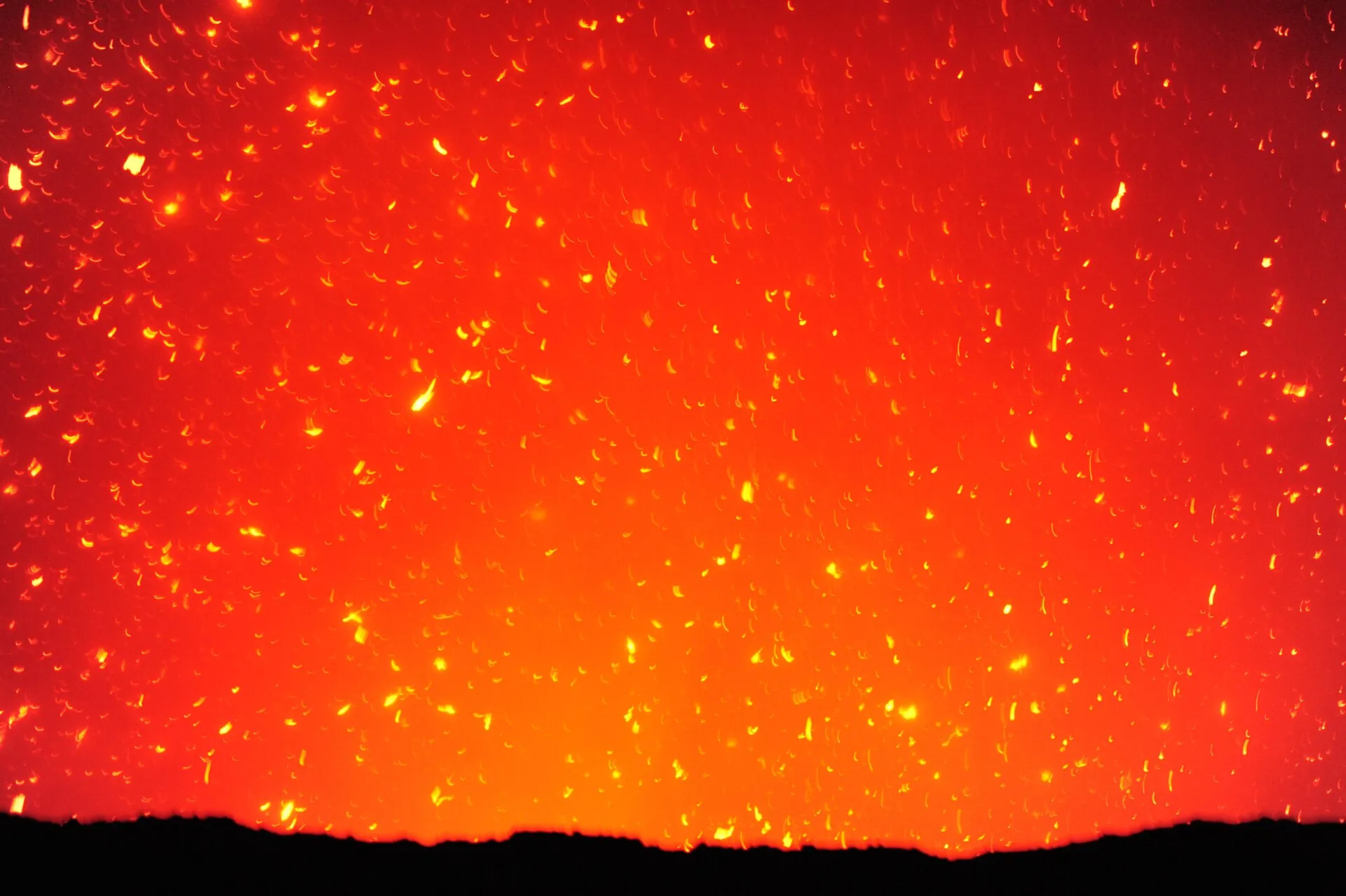 Nächtliche Explosion im Krater des Mount Yasur: glühende Lavafetzen fliegen über den Kraterrand