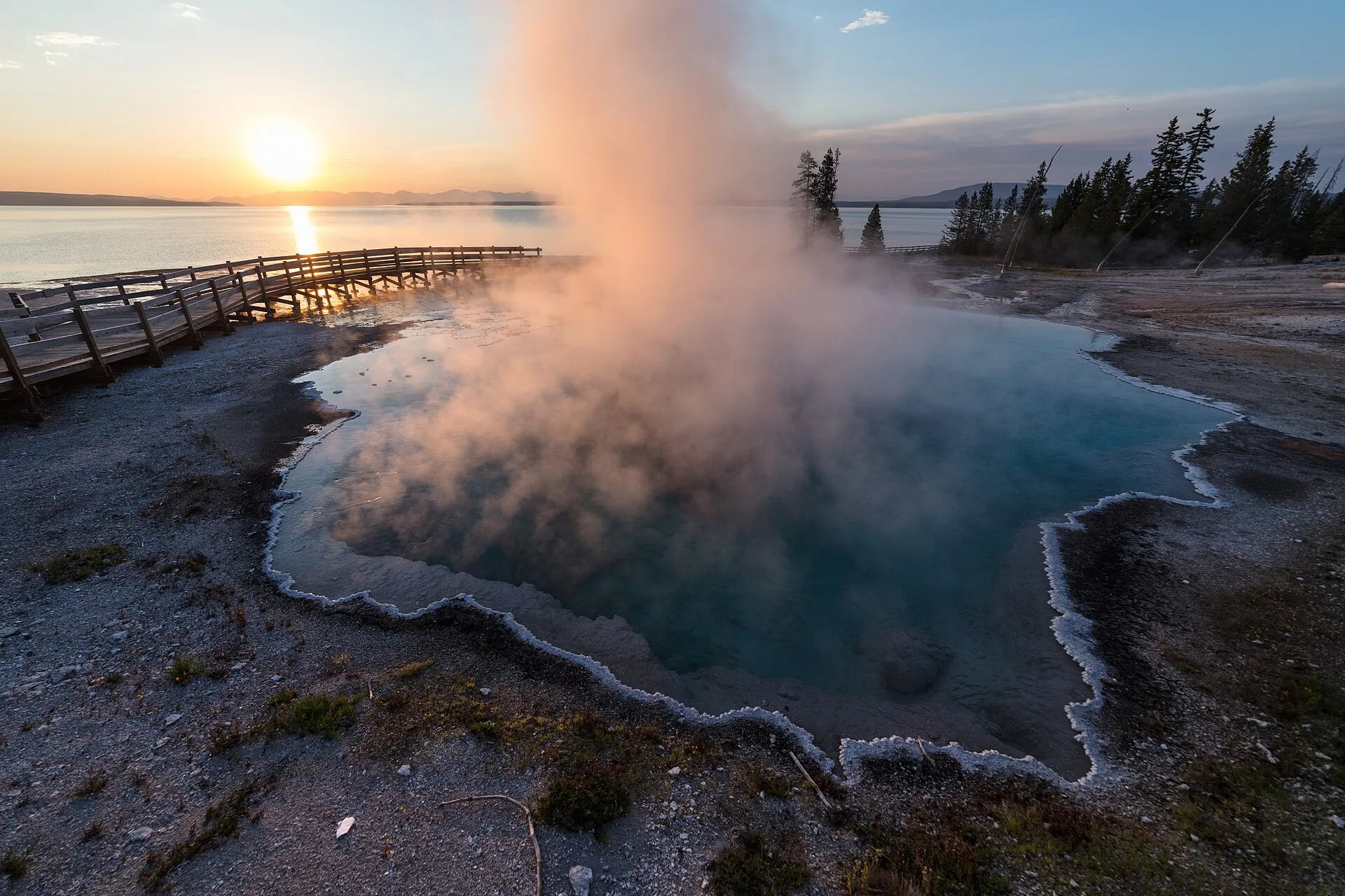 Black Pool im West Thumb Geyser Basin des Yellowstone bei Sonnenaufgang: Dampf über der türkisfarbenen heißen Quelle, dahinter der Bohlenweg am Yellowstone Lake